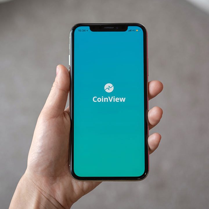 A person holding an iphone with coinview logo on it.