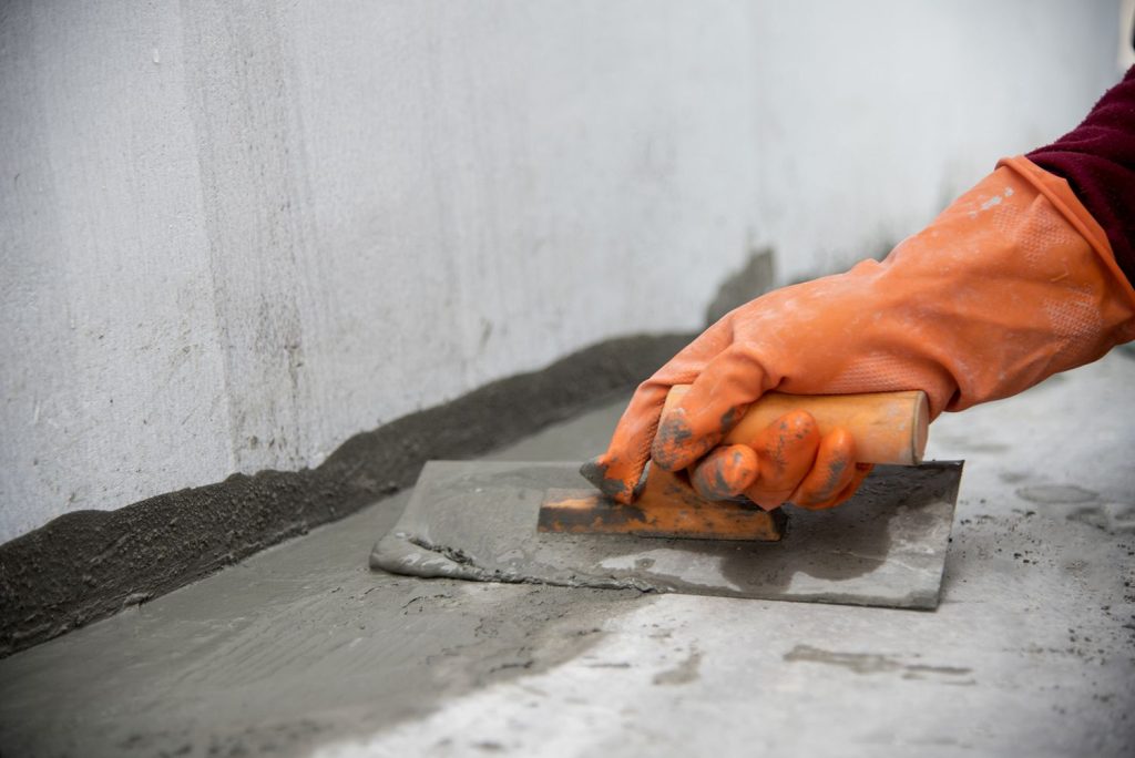 A person with orange gloves is working on cement.